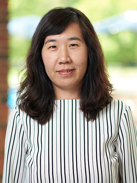 Portrait of Jing Gao. She is wearing a striped top and standing in front of the windows in the atrium of MSEE.