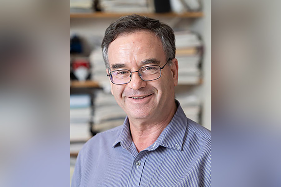 Portrait of Professor Sabre Kais. He is waring glasses and a blue button up shirt and standing in front of a blurry background of books in an office.