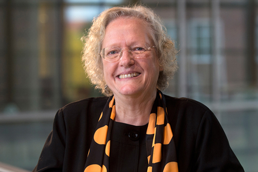 Portrait of Leah Jamieson in the atrium of the Armstrong building. She is wearing glasses, black top, and a gold and black scarf.