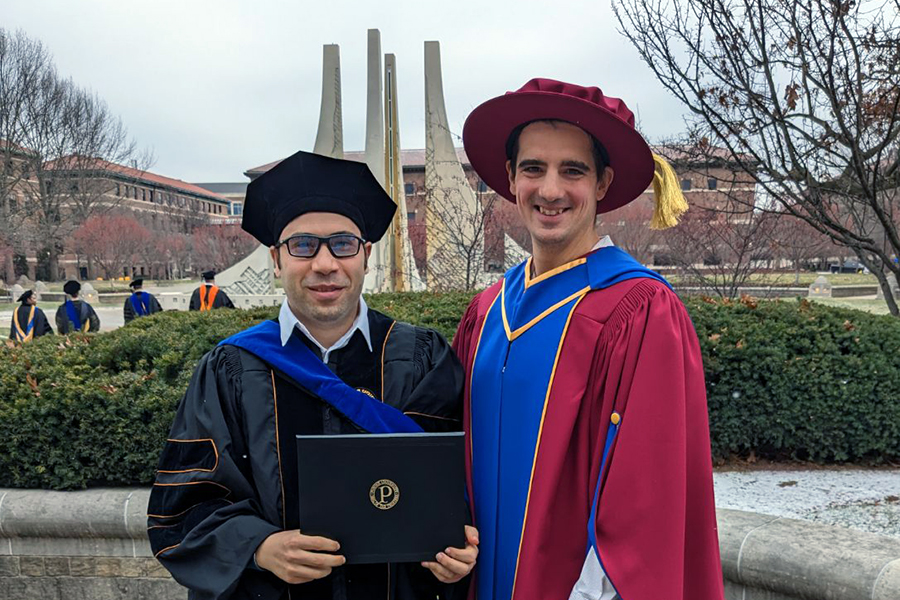 Mahmoud Khairy is wearing his graduation regalia standing next to Professor Tim Rogers who is wearing his own. They are standing together with the Purdue Engineering fountain in the background.