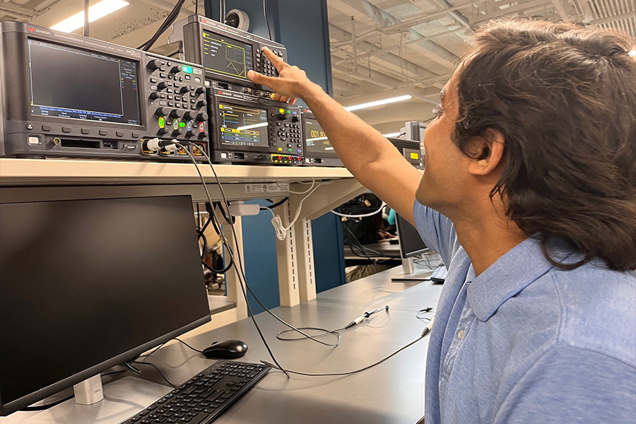 A man focused on an oscilloscope in a laboratory setting, surrounded by scientific equipment and research materials.