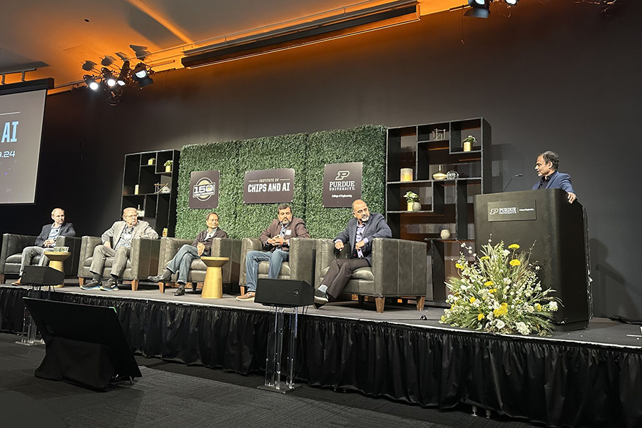 Conference stage featuring a panel of speakers, with attendees seated and participating in the event