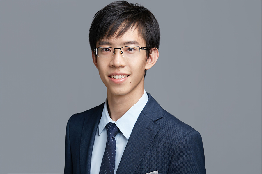 A young man in a suit and tie stands confidently, posing for a professional photo with a pleasant expression.