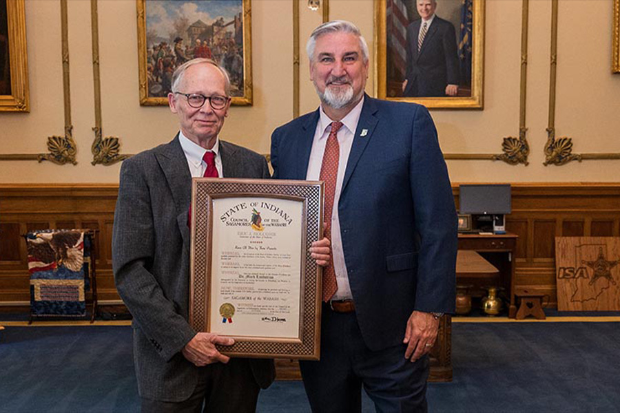 Two men in business suits stand together, each holding a framed certificate that signifies their achievement.