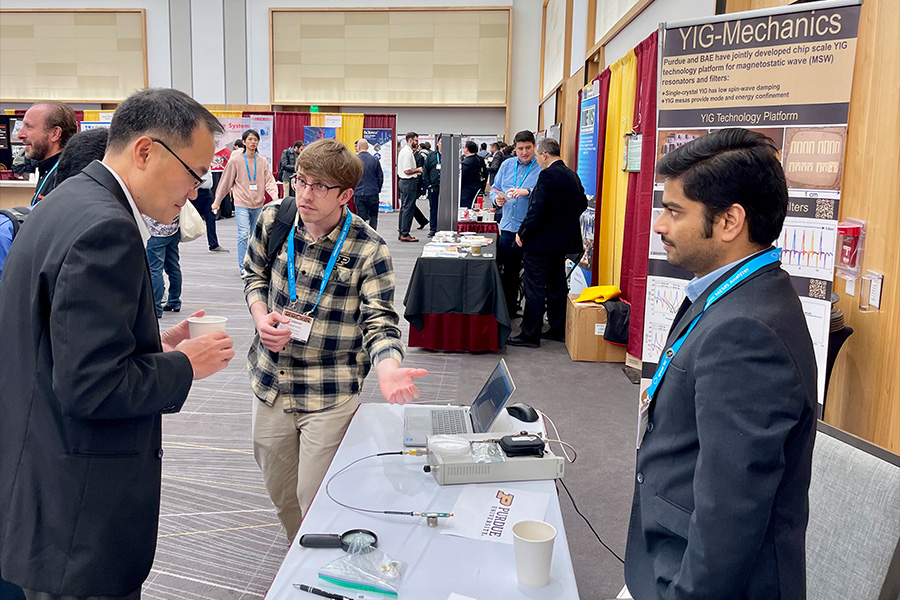 Two men engaged in discussion at a table, with a laptop and other equipment placed in front of them
