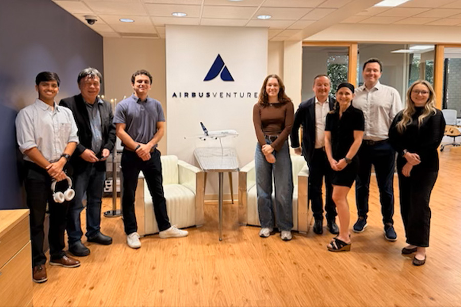 A group of eight people stand smiling in an office with "Airbus Ventures" on the wall. They're casually dressed, suggesting a relaxed, professional atmosphere.