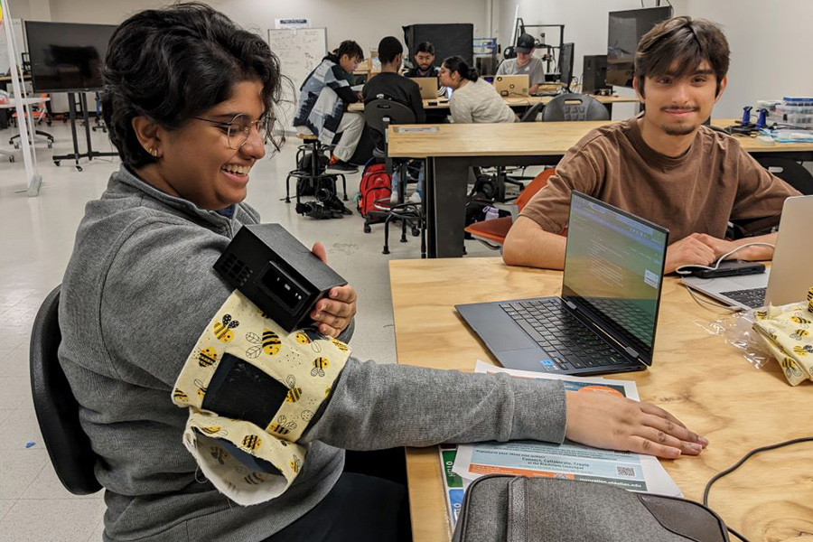 Student wearing a device on her right arm like a blood pressure sleeve, with a pattern designed with bee icons