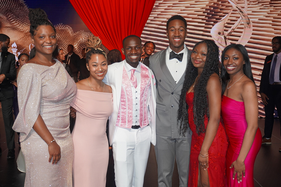 Group of six students wearing dresses and suits, posing, smiling for photo inside NSBE convention hall