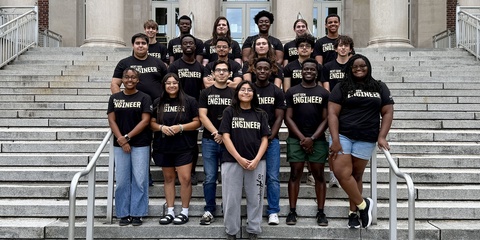 A group of students wearing black T-shirts that say "think summer," standing on the steps to Hovde