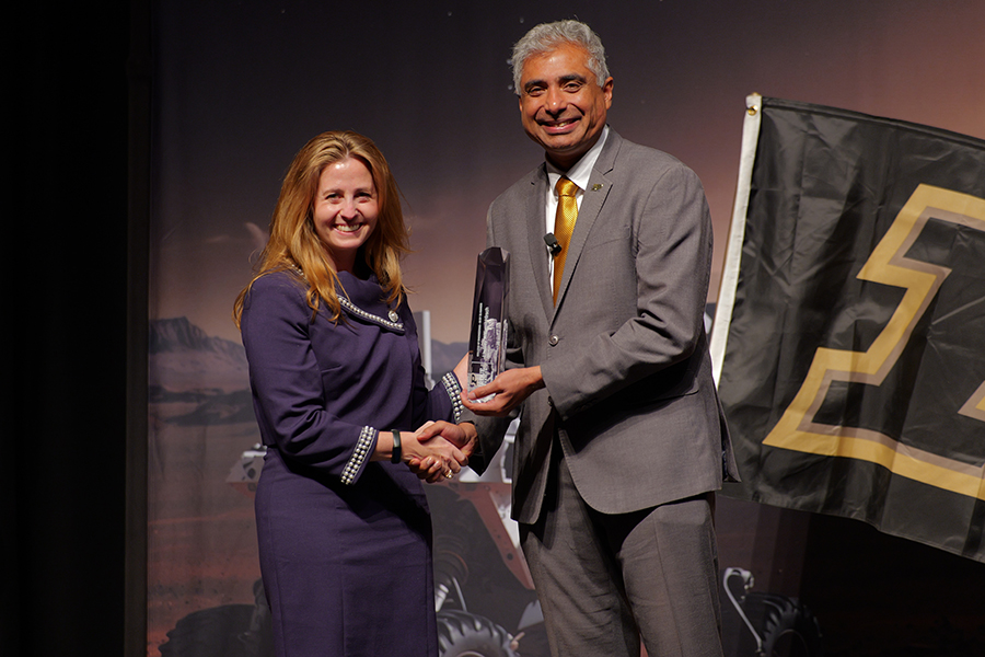 Woman with long blonde hair, smiling, holding trophy and shaking hand of man