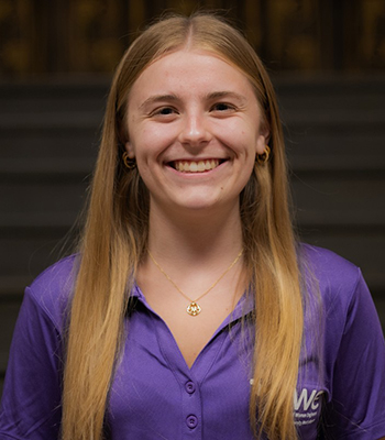 Student with blonde hair, smiling, wearing purple SWE polo, head shot