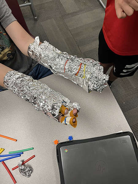 A student holding arms in front, wrapped in foil, as part of activity